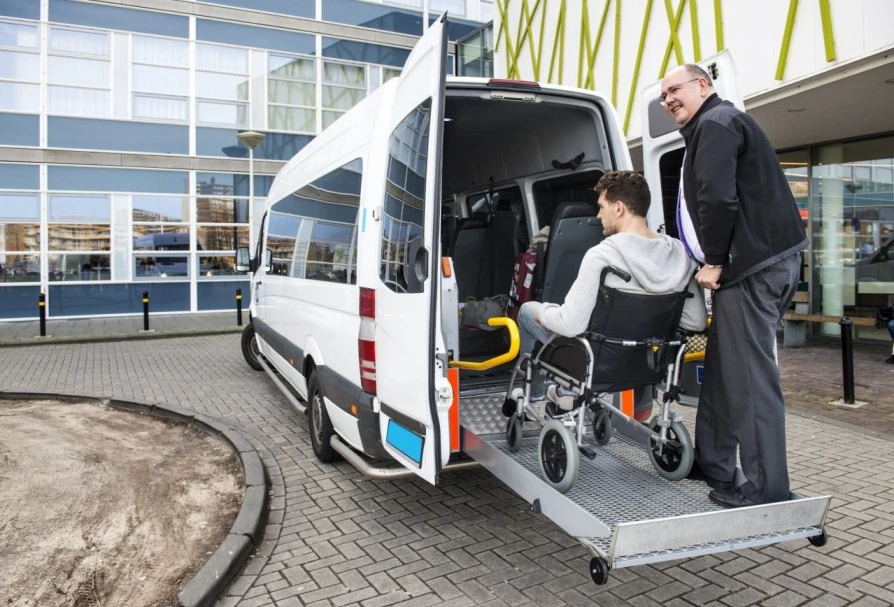 Carer helping man in wheelchair into van