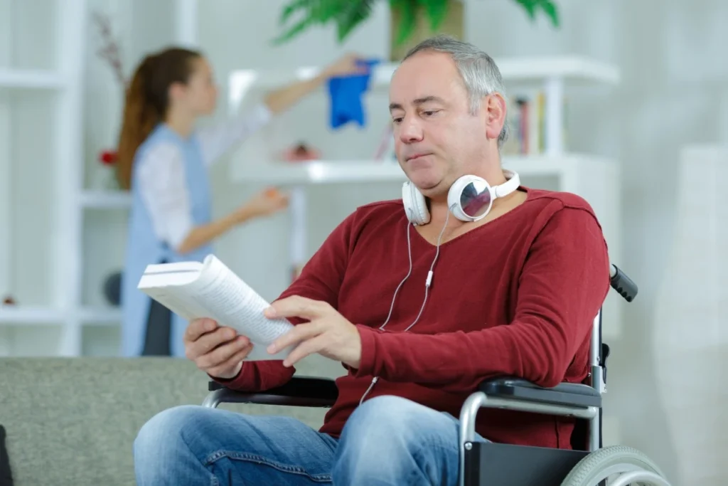 Man in wheelchair with carer cleaning in the background